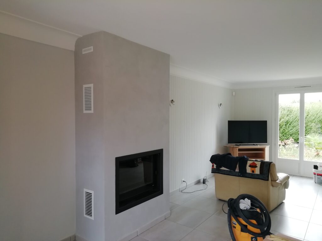 Salon moderne gris clair avec cheminée design et insert noir, murs lambrissés, sol carrelé, grande baie vitrée sur jardin verdoyant.