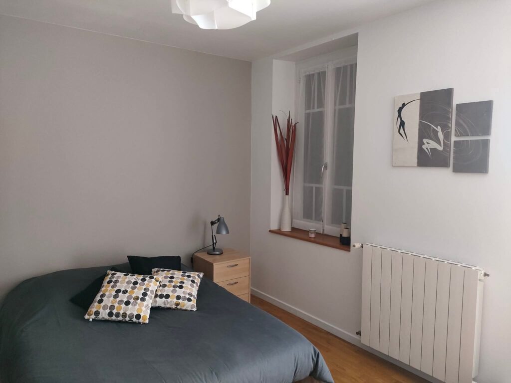 Chambre à coucher moderne avec lit gris, table de chevet bois, fenêtre lumineuse et décoration murale minimaliste.