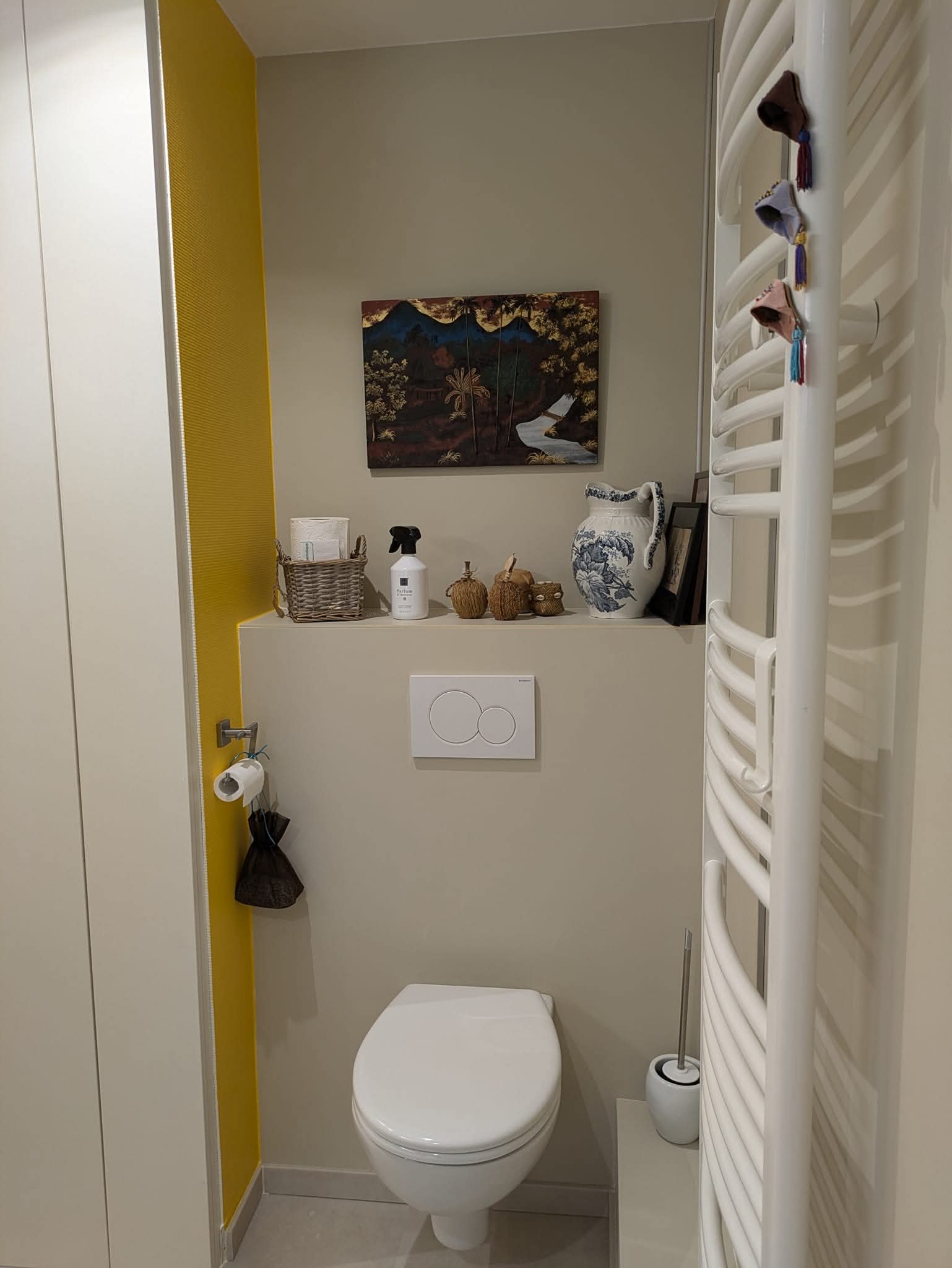Toilette suspendue moderne, mur jaune vif, étagère décorée de bibelots et sèche-serviettes blanc dans un petit WC chic.