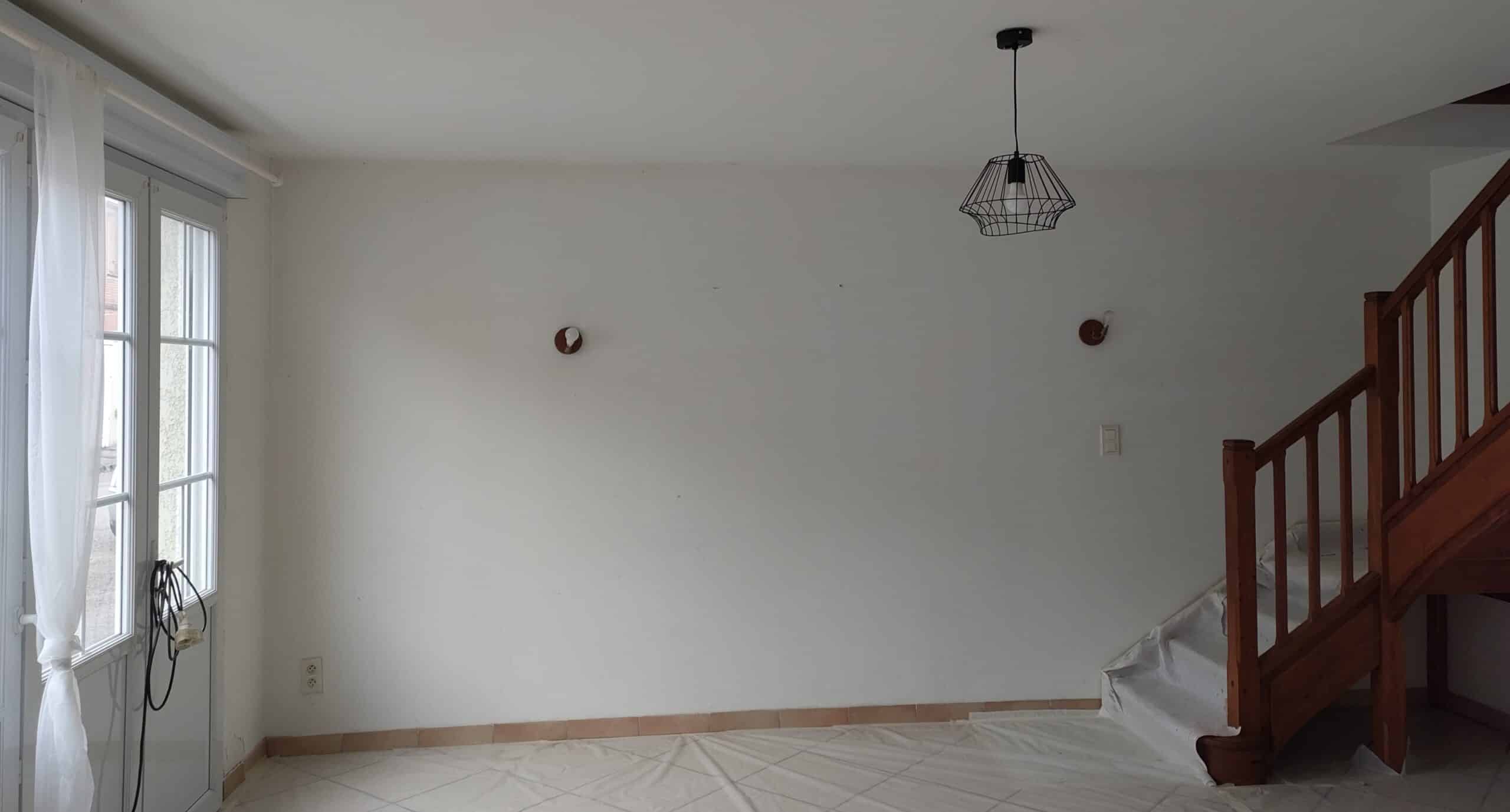 Mur blanc vide avec escalier en bois, suspension noire et bâches de protection pour rénovation intérieure.