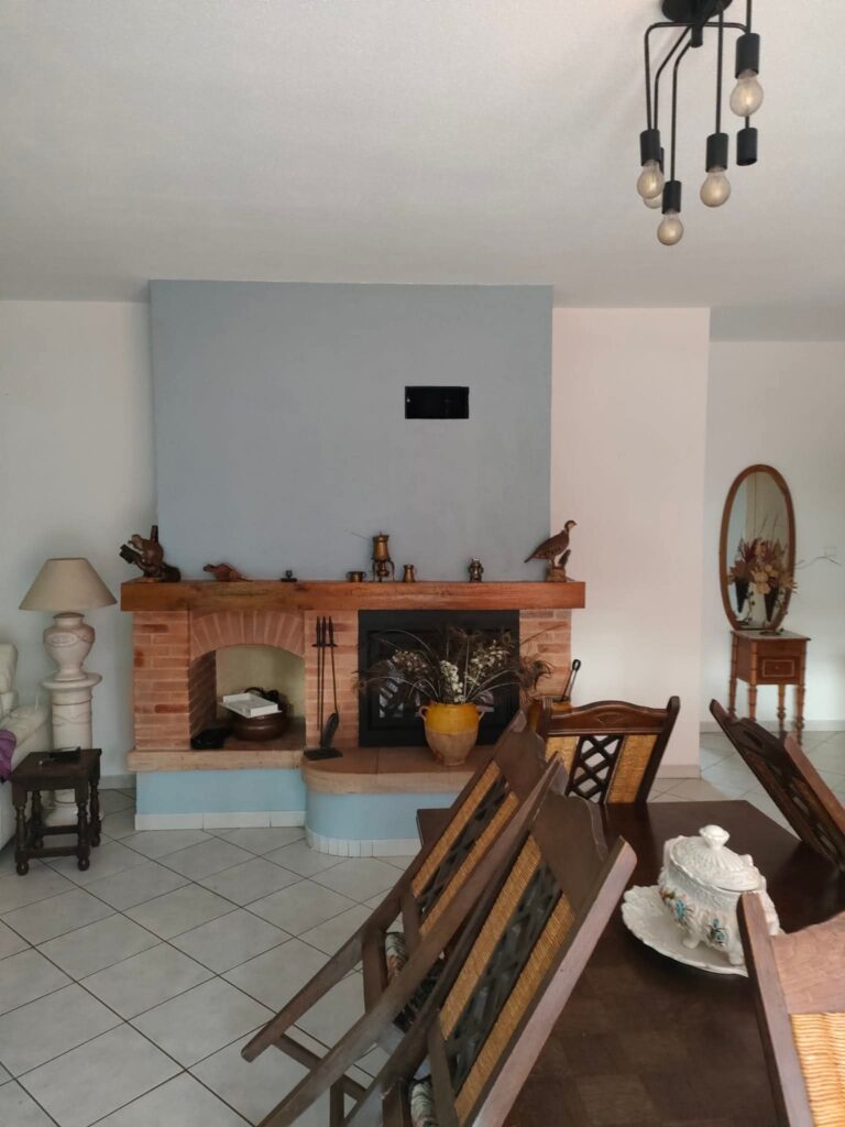 Salon rustique avec cheminée en brique, table à manger en bois massif et lustre design noir au plafond.
