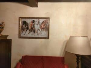 Tableau de quatre chevaux galopant au-dessus d'un canapé rouge capitonné dans un salon chaleureux.